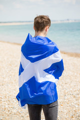 Caucasian male on a beach holding a Scottish flag