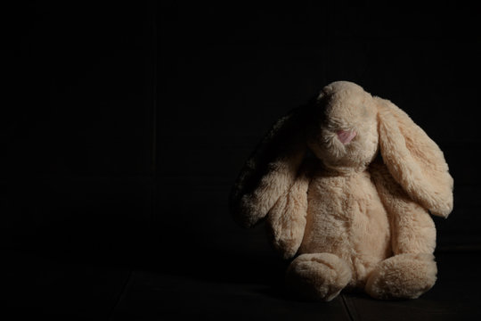 Soft toy  rabbit on a dirty dark background in the beam of hard light with shadow. Lost childhood concept