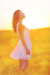 Fototapeta na wymiar Young woman on field under sunset light