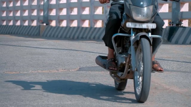 The wheels of the motorcycle go on the asphalt road and bounce on a bump 