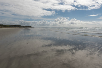 The sky and clouds reflected in the wet sands of the beach at Karikari Moana, Northland, New Zealand.
