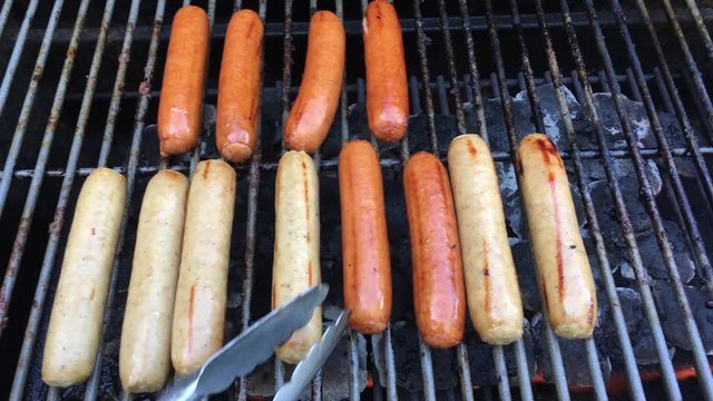 Turning brats on an outdoor propane grill with thongs.