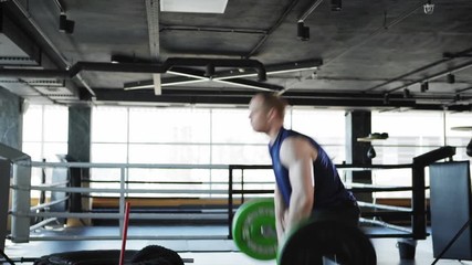 Side view medium shot of determined middle aged man doing overhead barbell lifts and box jumps exercise in gym workout