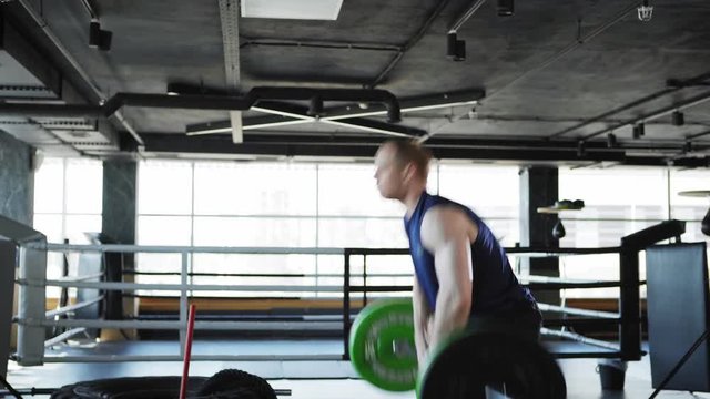 Side view medium shot of determined middle aged man doing overhead barbell lifts and box jumps exercise in gym workout
