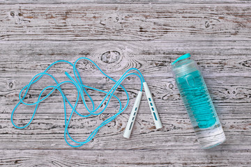 Blue jump rope and blue water bottle on wooden background. Sports style. Flat lay.