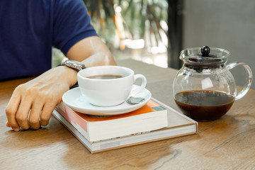 Man sits on table with coffee on the book in coffee shop.