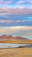 Fototapeta na wymiar Vertical Panorama of a calm lake with vast sandy shore under cloud filled sky