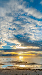 Vertical frame Striking cloudy sky over a calm lake that reflects the golden sun at sunset