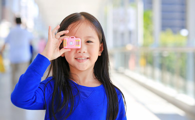 Fototapeta premium Adorable little Asian girl using a toy camera to take pictures outdoor. Kid development concept.
