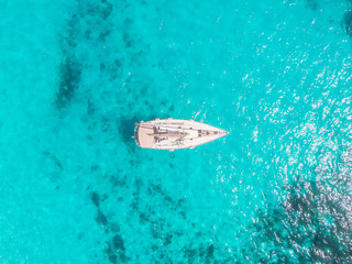 Aerial top view white yacht with sail stands on coral reef in blue transparent turquoise sea....