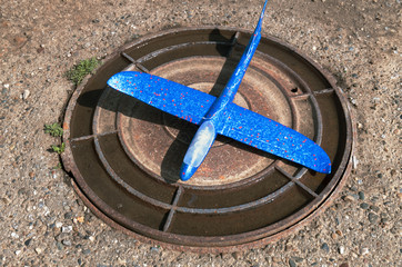 Blue toy airplane on steel round manhole cover.