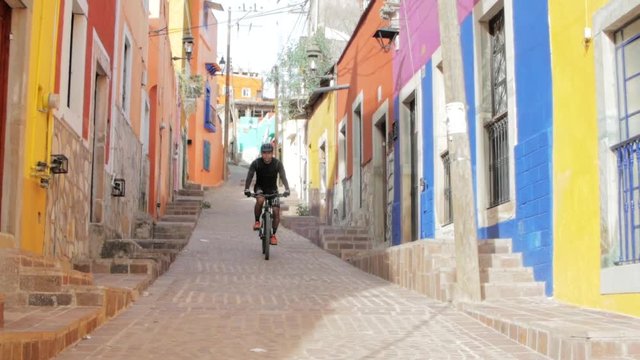 Hispanic man on a mountain bike descending from a colorful alley. Downhill cyclist on the streets of the city. 