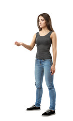 Young woman in gray top and blue jeans standing in half-turn, one arm bent with palm facing up as if holding something on white background.