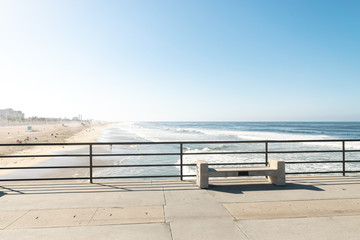 Concrete bench on pier overlooking beach, ocean, and blue skies at sunrise