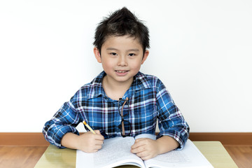 Asian boy without glasses doing his homework on the table with white background