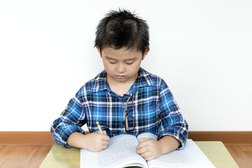 Little student boy without glasses doing his homework on the table with white background