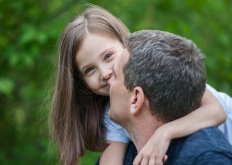 Fototapeta premium Portrait of cute little girl held in father's arms. Happy loving family. Father and his daughter child girl playing hugging. Cute baby and daddy. Concept of Father day. Family holiday and togetherness