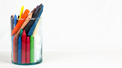 Fototapeta premium Many colourful crayon and School Supplies in glass bowl, isolated on a white surface.