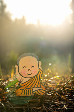 photo of a little boy in the early morning at sunrise in the green grass(figure, doll) .  Hands up, Happy smiling face. Close-up, blurred green background, free space for text.