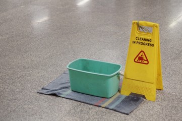 Yellow Caution wet floor cleaning in progress sign on wet floor with green bucket