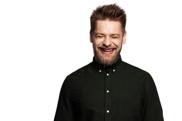 Portrait of laughing young man smiling with closed eyes. Fashionably dressed in black shirt guy in good mood in studio. Copy space in left side. Happiness concept. Isolated on white