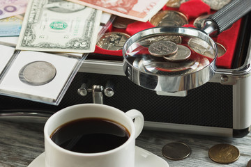 Different old collector's coins and banknotes with a magnifying glass and cup of coffee