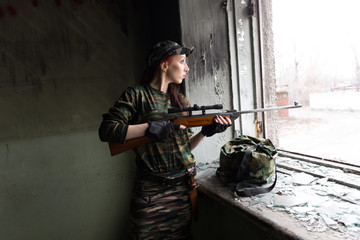 A thin red-haired girl stands at the broken window with a rifle. The girl in green camouflage with...