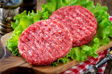 Raw mince meat beef burgers on a wooden cutting board with lettuce leaves