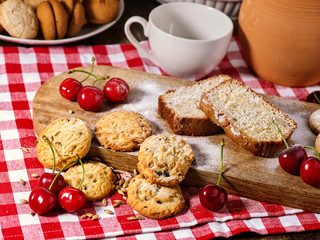 Oatmeal cookies and cherry on kitchen cutting board gingham checkered cotton fabric on table in village style for picnic with plate of macaron background. How to quickly replenish energy and vitality.