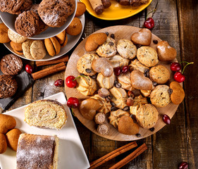 Oatmeal cookies and sand chocolate cake with cherry berry and crispy wafer rolls with cream on cutting board on wooden table in rustic style. Limitations for diabetics. Perfect for breakfast.