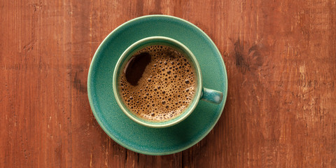 A panoramic view of a cup of black coffee on a dark rustic wooden background, shot from the top with a place for text