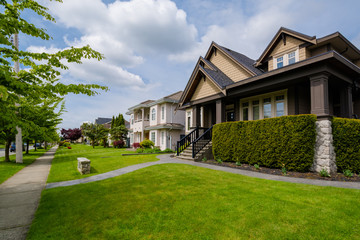 Fototapeta na wymiar Street of residential houses with concrete pathways and green lawns in front on cloudy day in Vancouver, Canada