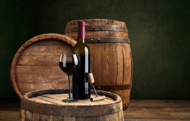 Bottle and glass of red wine on wooden barrel shot with dark wooden background
