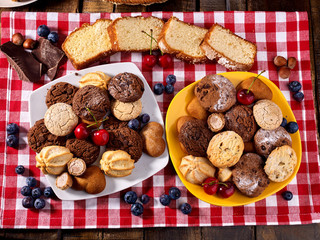 Oatmeal Cookies and sand chocolate cake with blueberries on wooden table with gingham cloth in farm style close up. Table setting breakfast for two with cups in. Best range of confectionery products.