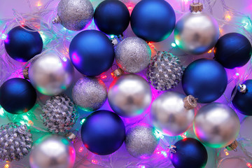 Christmas balls in blue and white colors wiht lighted garland decoration on lilac background