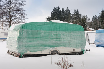 Camper covered with plastic and protective tarp in winter season