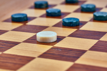 Malachite checkers and one marble checker on a wooden checkerboard. Close-up
