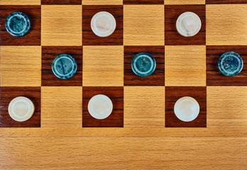 Malachite checkers and marble checkers on a wooden checkerboard. Flat lay