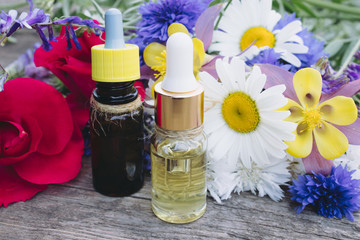Natural essential oil with wild flowers on wooden background.