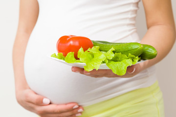 Young woman's hand holding plate of fresh vegetables. Healthy eating, receiving vitamins in pregnancy time. Closeup.