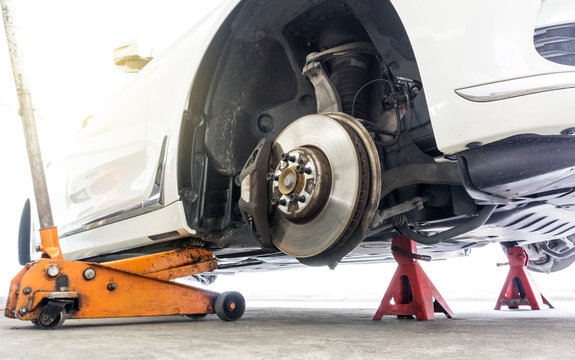 Car without wheel on car jack with car stands for safety in repair shop background.