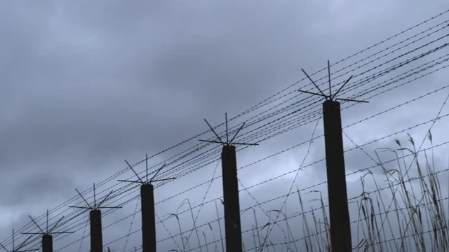 Panning shot of a barbwire fence of a prison camp on a gray and stormy day