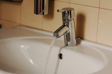 Water from the tap. A stream of clean water flows into the sink. Open chrome faucet washbasin. Warm...