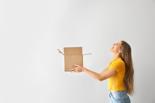 Young woman with open cardboard box on light background
