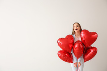 Beautiful young woman with heart-shaped air balloons on light background