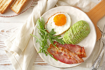 Plate with tasty fried egg, avocado and bacon on wooden table