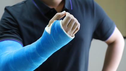 Closeup of Asian man's arm with long arm plaster, fiberglass cast therapy cover by blue elastic...