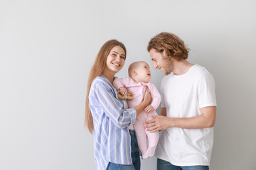 Happy parents with cute little baby on light background