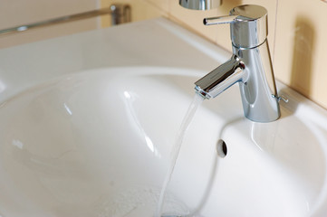 Water from the tap. A stream of clean water flows into the sink. Open chrome faucet washbasin. Warm...