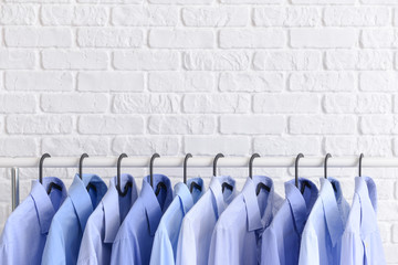 Rack with clothes after dry-cleaning near white brick wall